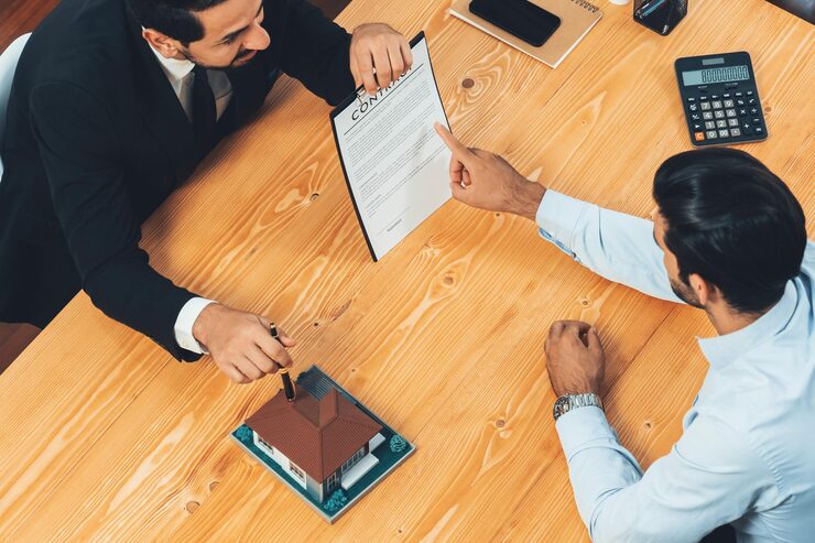 two-men-sitting-desk-with-document-that-says-real-estate_31965-99995